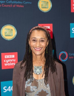 Actress Suzanne Packer smiling in front of a branded step and repeat media wall at an event, photographed by South Wales event photographer Charlie Hannah