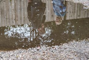Close-up frame focusing tightly on the upside-down reflection of TV production cast members in a puddle of water.