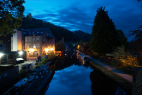 Fine art canal photography by Charlie Hannah ARPS, capturing a deep blue twilight sky over a canal flanked by warmly lit historic brick buildings and a dark silhouette of a tree.
