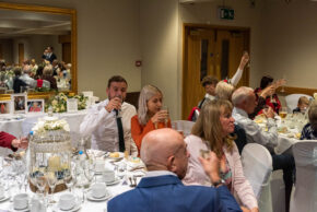 Wedding guests raising a glass and enjoying drinks during the wedding breakfast reception, captured candidly by South Wales wedding photographer Charlie Hannah.