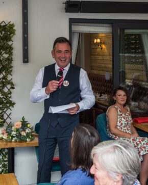 Groom laughing while delivering a speech holding notes and a microphone during the Pamela and Philip wedding reception, photographed by Charlie Hannah