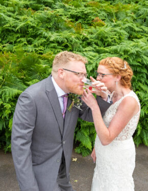 Bride and groom playfully linking arms to drink from their champagne glasses outdoors, photographed by South Wales wedding photographer Charlie Hannah